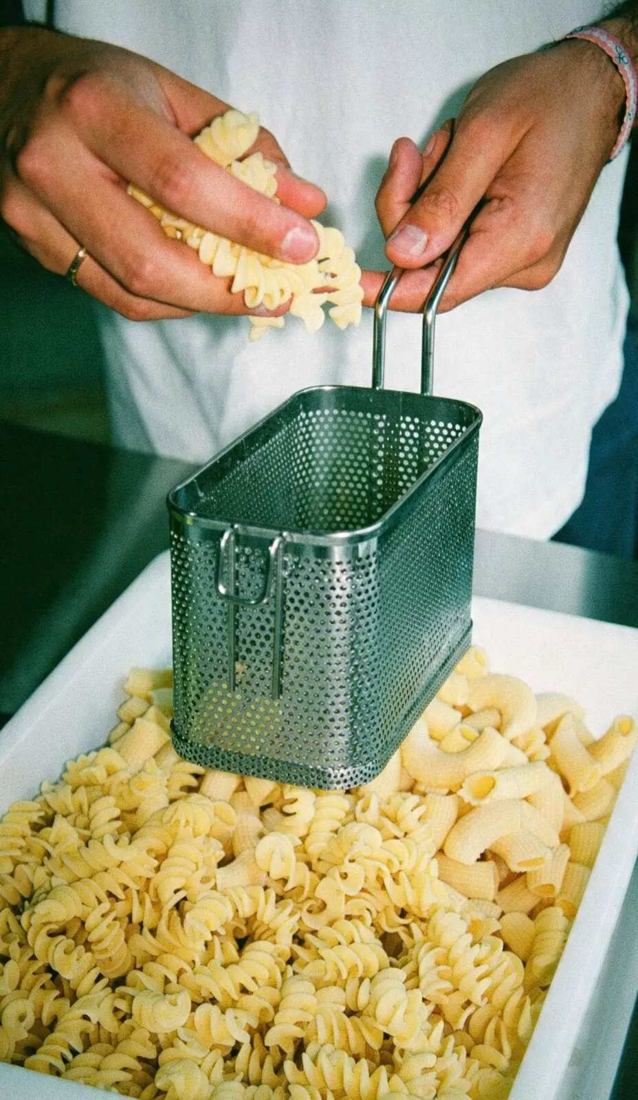 Manos echando pasta fresca en el cestillo para cocerla al momento